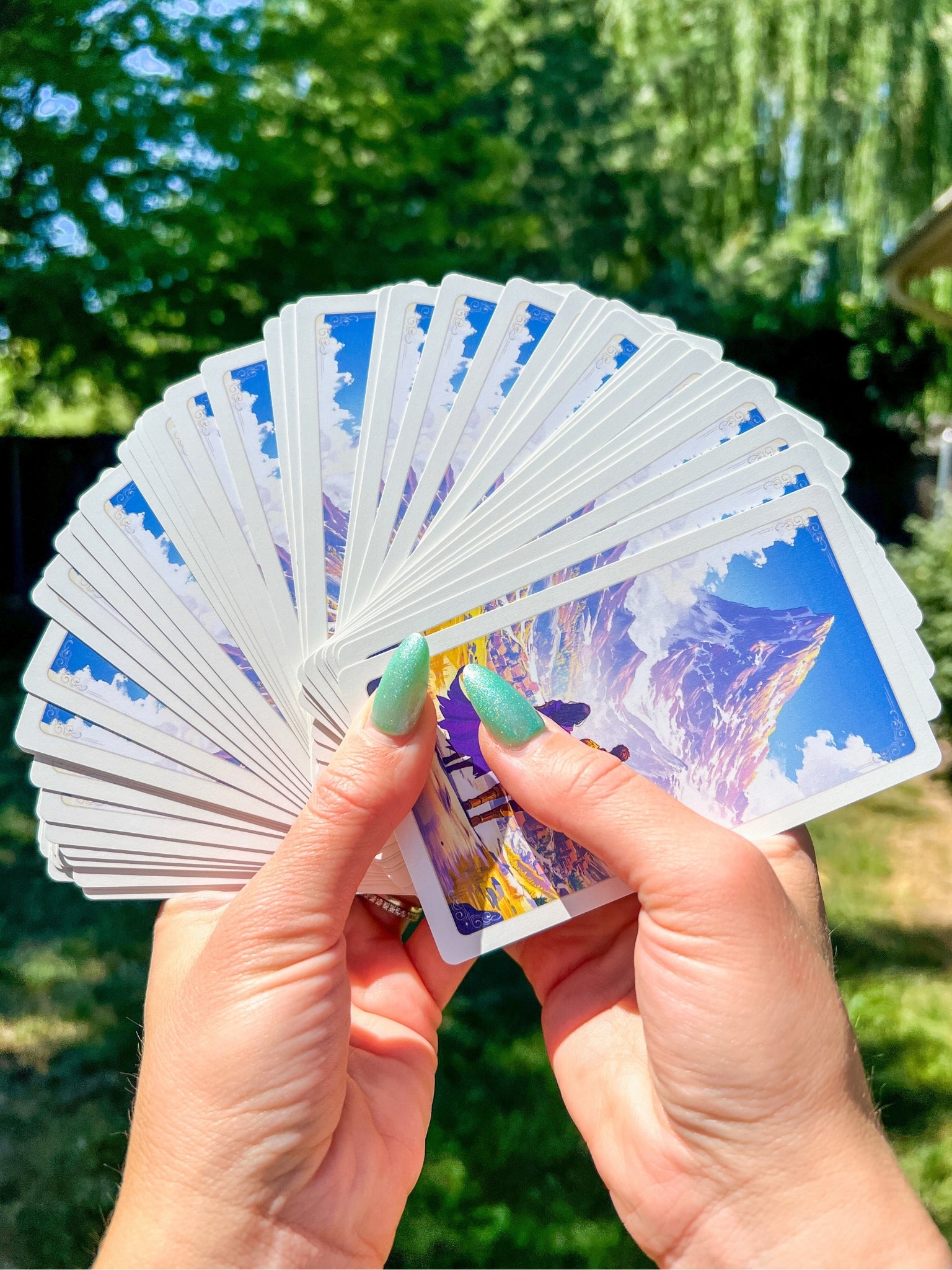 Fanned-out deck of self-care cards held by hands in a relaxing outdoor setting.
