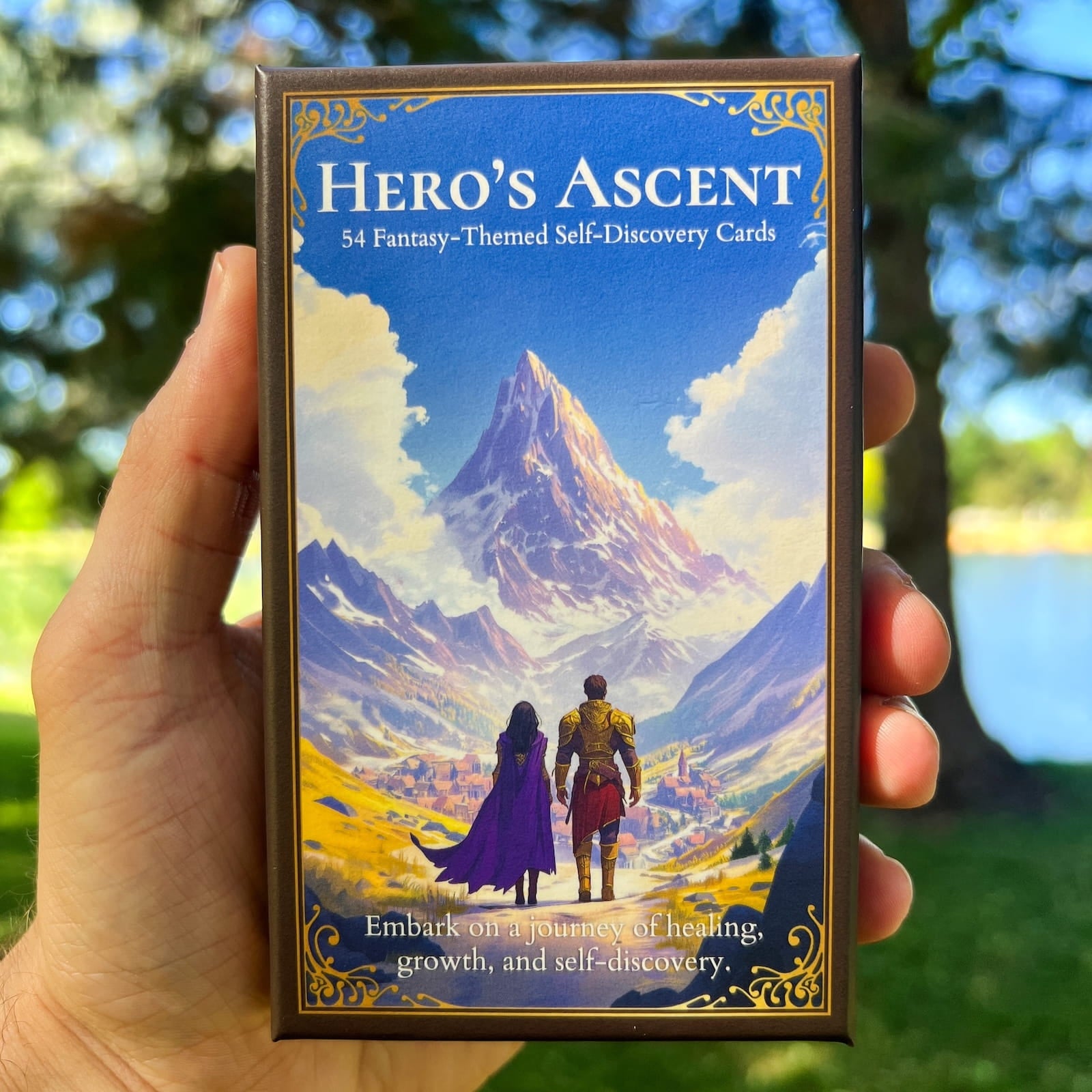 A fantasy-themed self-discovery card deck titled 'Hero's Ascent' held by a hand outdoors with a scenic forest background.