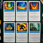 Six fantasy-themed self-discovery cards arranged in a 2x3 grid on a dark green textured surface with small decorative props at the corners. The cards feature colorful illustrated artwork and blue title banners reading titles such as The Enchanted Forest, The Hero's Sword, The Phoenix, The Rebel's Mask, The Orc's Fury, and The Bard's Melody.