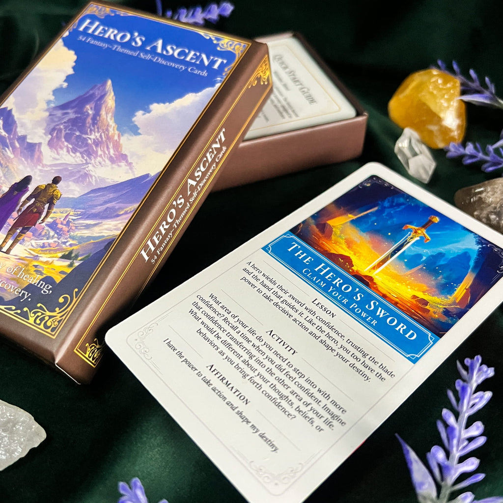 A boxed oracle card deck titled "Hero's Ascent" shown with one card laid out on a dark green surface. The box and card feature fantasy artwork with blue, gold, orange, and purple tones, and the scene is styled with crystals and purple flowers.