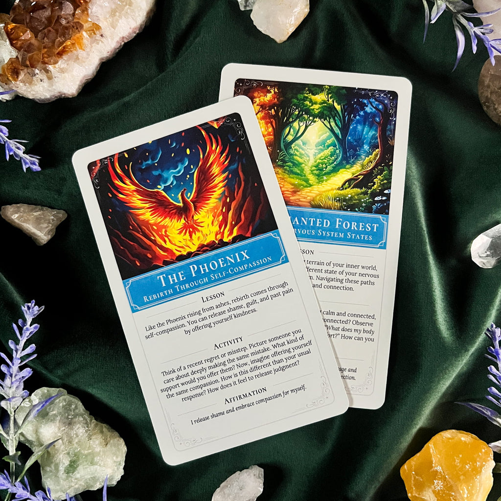 Two oracle cards, titled 'The Phoenix' and 'The Wanted Forest', are displayed on a dark green velvet cloth surrounded by crystals and purple flowers. The cards feature vibrant, colorful illustrations of a fiery phoenix and a glowing forest, with text boxes below the artwork.