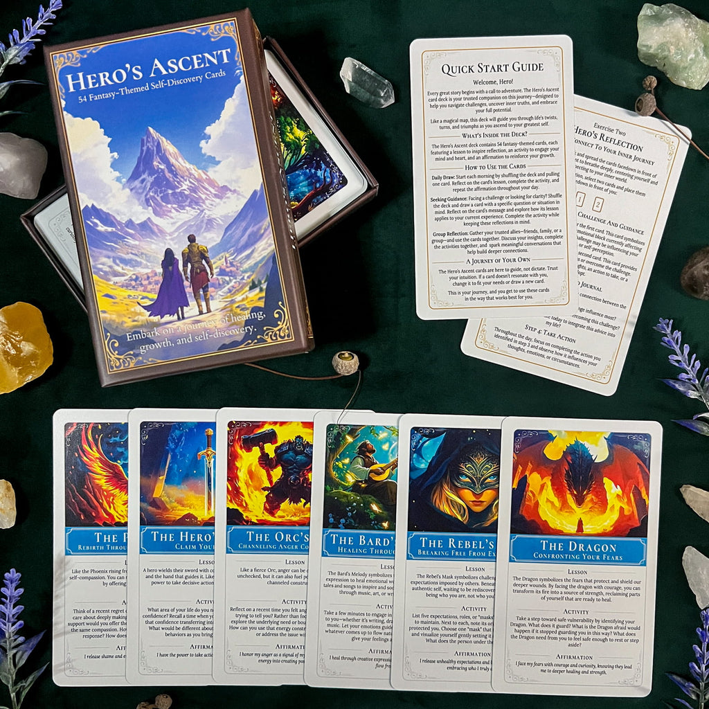 A Hero's Ascent card deck is displayed on a dark green cloth with several illustrated cards spread out in front. The box shows fantasy artwork of a mountain landscape with two figures, and the cards feature colorful scenes such as fire, storm, forest, and dragon imagery.
